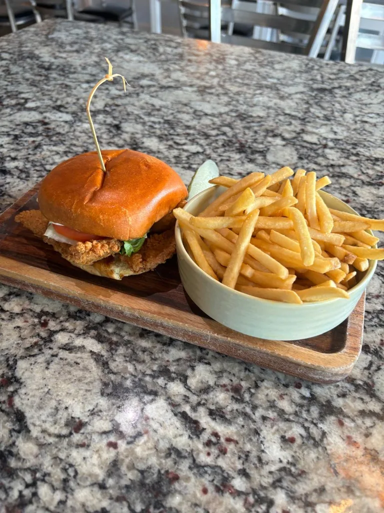 Crispy catfish sandwich on a brioche roll with lettuce, tomato, tartar sauce, served with french fries and pickle at Estime's Cafe Colonia NJ